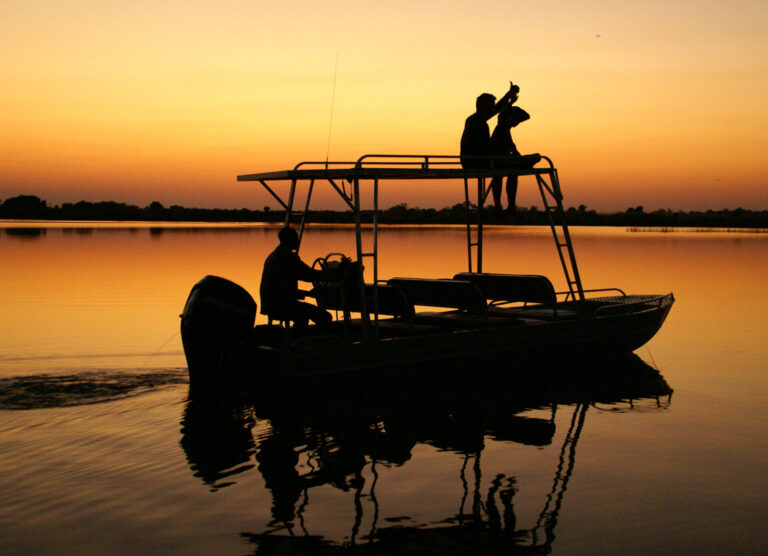 Safari boat at sunset on calm Okavango Delta waters near Kwara Camp.