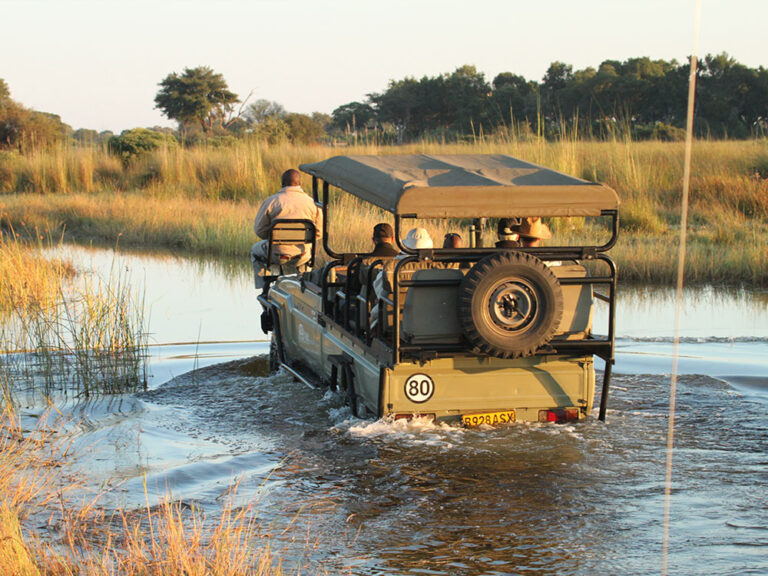 Safari vehicle crossing a shallow water channel at Kwara Camp.