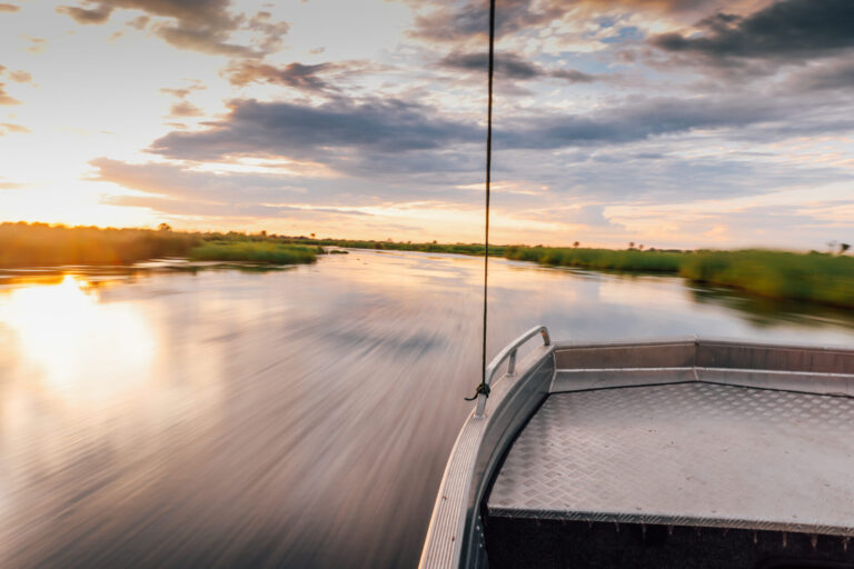 Boat gliding through Okavango Delta waters during sunset.