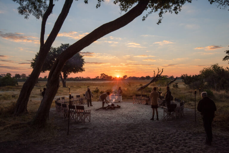 Guests gathered around a campfire under a glowing sunset sky at Splash Camp.