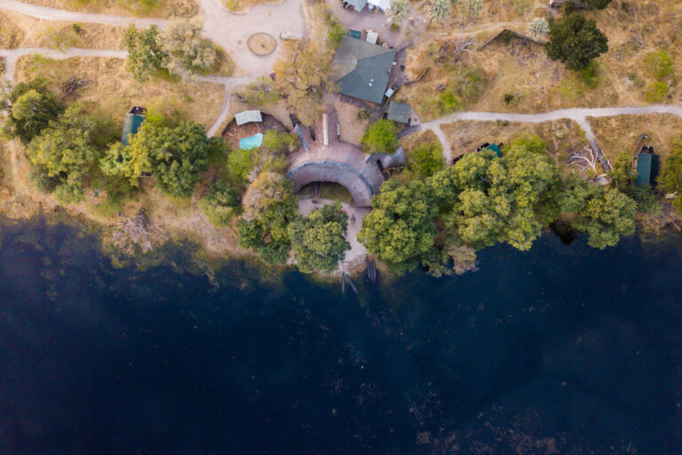 Aerial view of Pom Pom Camp beside a blue lagoon in the Okavango Delta.