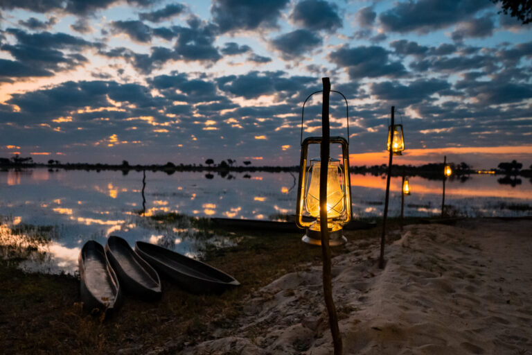 Lit lanterns and mokoro canoes beside the lagoon at sunset at Pom Pom Camp.