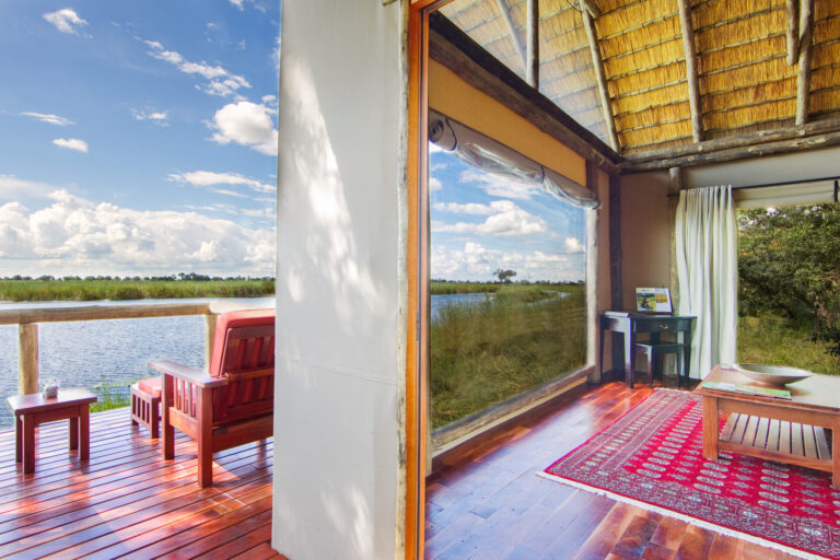 Open safari tent suite with wooden floors and view of lagoon from private deck.