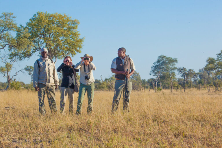 Group of safari guides and guests standing in grassy plains near Lagoon Camp.