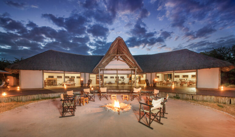 Thatched main lodge with open fire pit and seating area at Nxai Pan Camp.