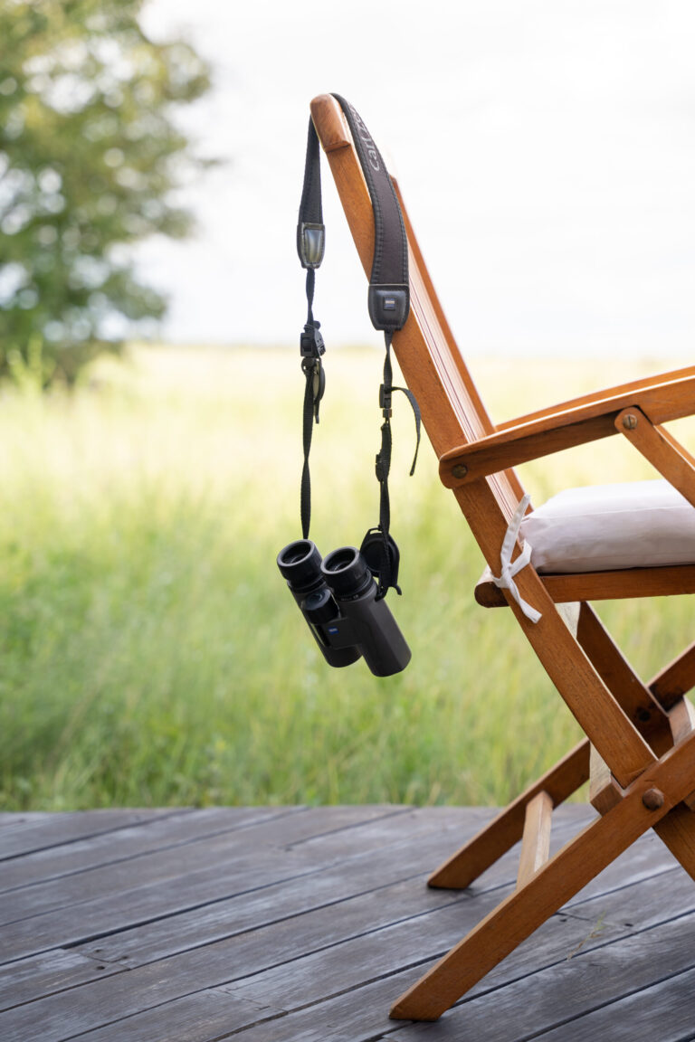 Pair of binoculars hanging on a wooden safari chair overlooking the grasslands at Nxai Pan Camp.