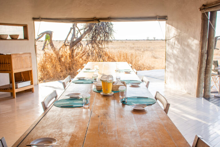 Sunlit dining table set for guests with views over the dry plains at Nxai Pan Camp.