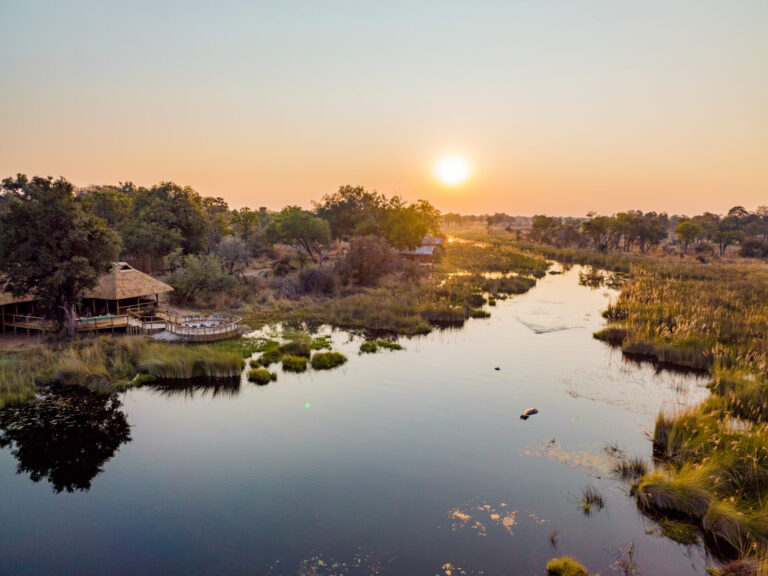 Aerial view of Four Rivers Camp beside a winding waterway at sunrise.