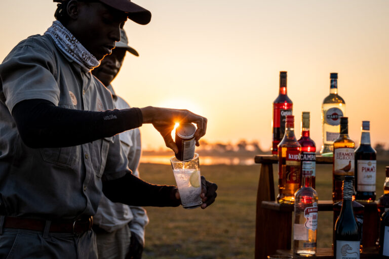 Guide pouring drink at sundowner setup in the Okavango Delta near Four Rivers Camp.
