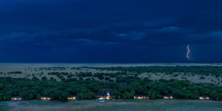Evening view of guest rooms at King Lewanika Lodge with dramatic stormy skies and lightning in the background