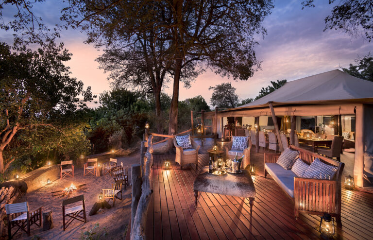 Sunset view from outdoor deck with lounge seating and lanterns at Linyanti Bush Camp in Botswana.