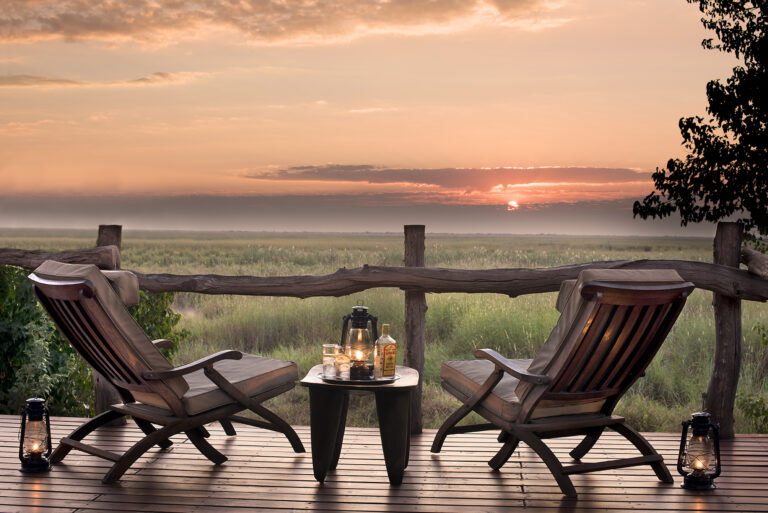 Two chairs and coffee table overlooking sunrise from a deck at Linyanti Bush Camp in Botswana.