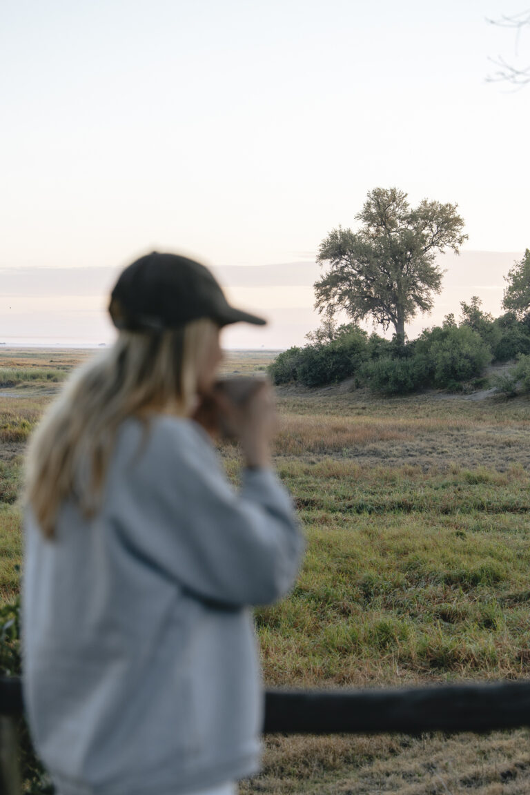 Guest drinking coffee and admiring the morning view from Linyanti Bush Camp in Botswana.
