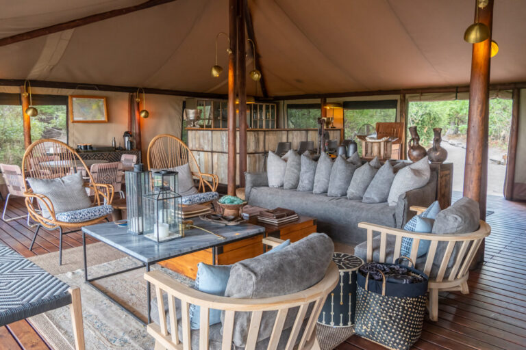 Main lounge with sofas, armchairs, and wooden decor inside Linyanti Bush Camp in Botswana.